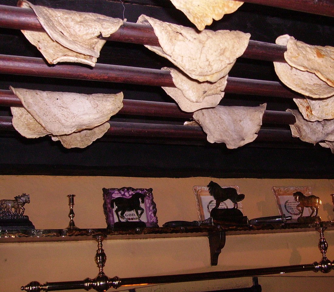 Soft oatcakes draped over wooden rails on a rack to dry, above a shelf of horse-brass ornaments