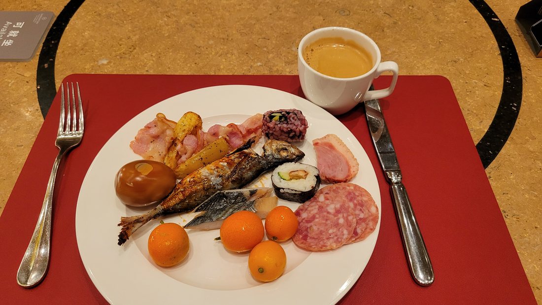 Grilled fish, cold cuts, a nori-wrapped roll, kumquats, a bread roll, and a cup of tea