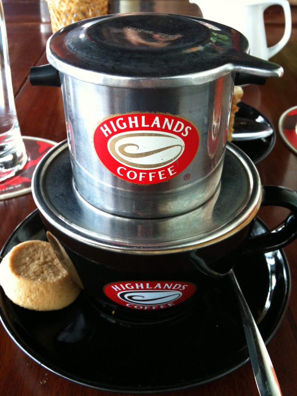 A phin sitting directly on the cup, lid on, dripping — stamped metal, four parts, no filter paper anywhere
