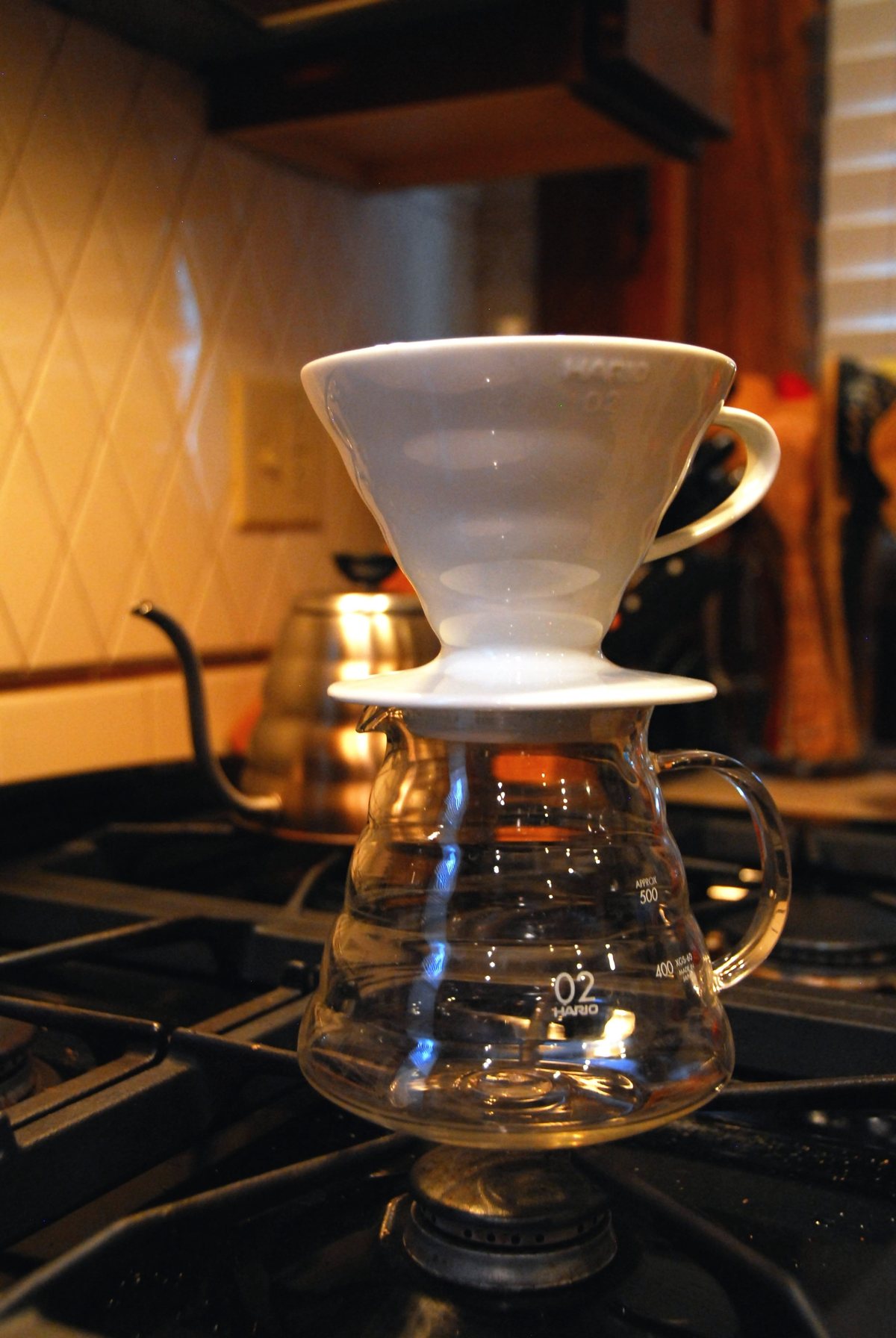 A ceramic Hario V60 cone seated on its glass server, gooseneck kettle waiting behind it — the 60° cone and spiral ribs are the whole design