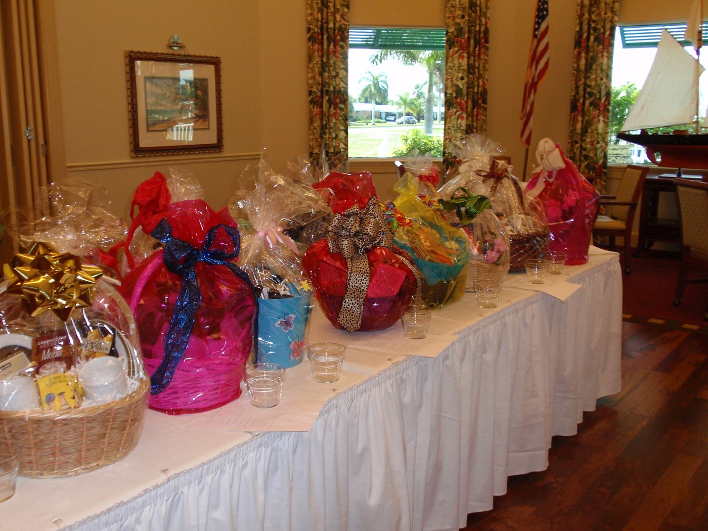 A long table with a white skirt, lined with gift baskets wrapped in clear and coloured cellophane and tied with bows