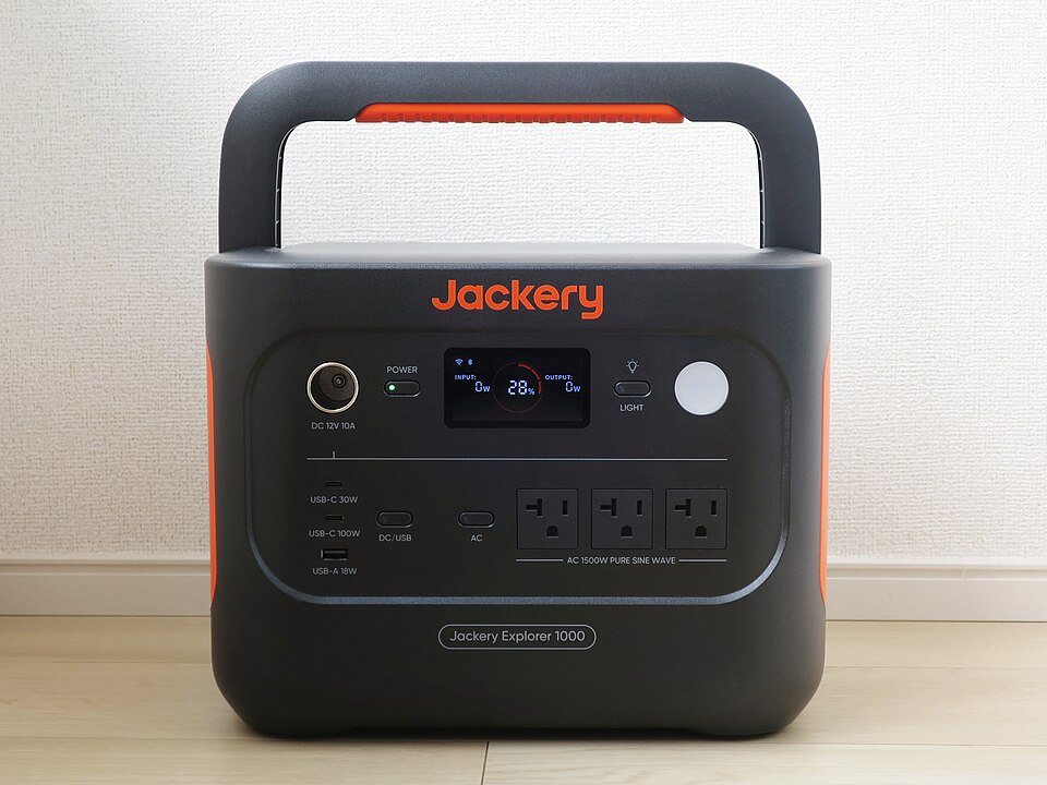 A grey and orange portable power station with a carrying handle, a display and three household outlets