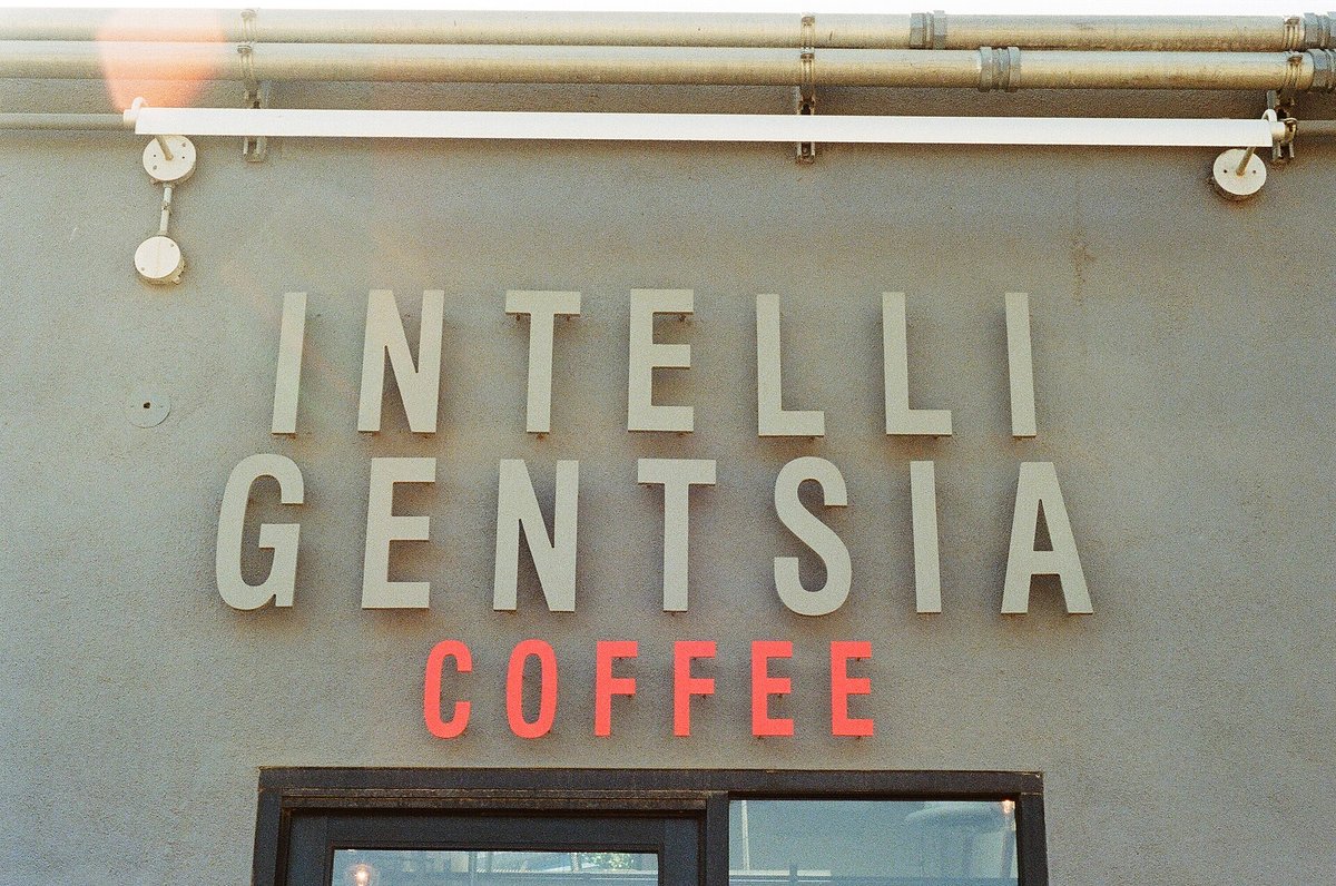 A grey building front with large raised letters reading Intelligentsia Coffee above the window, the word coffee in red