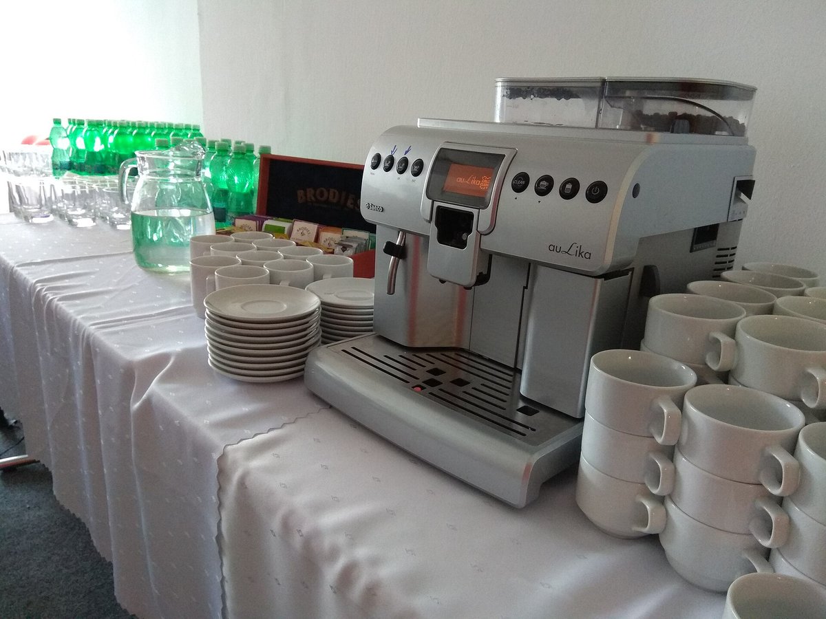 A white tablecloth event table with a bean-to-cup espresso machine, stacks of cups and saucers, and jugs of water