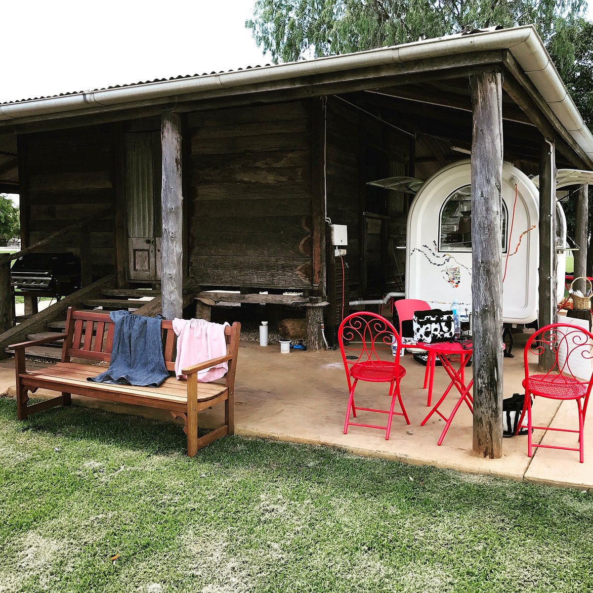 A small coffee cart under the veranda of a slab hut in a park, red chairs and a bench on the deck in front