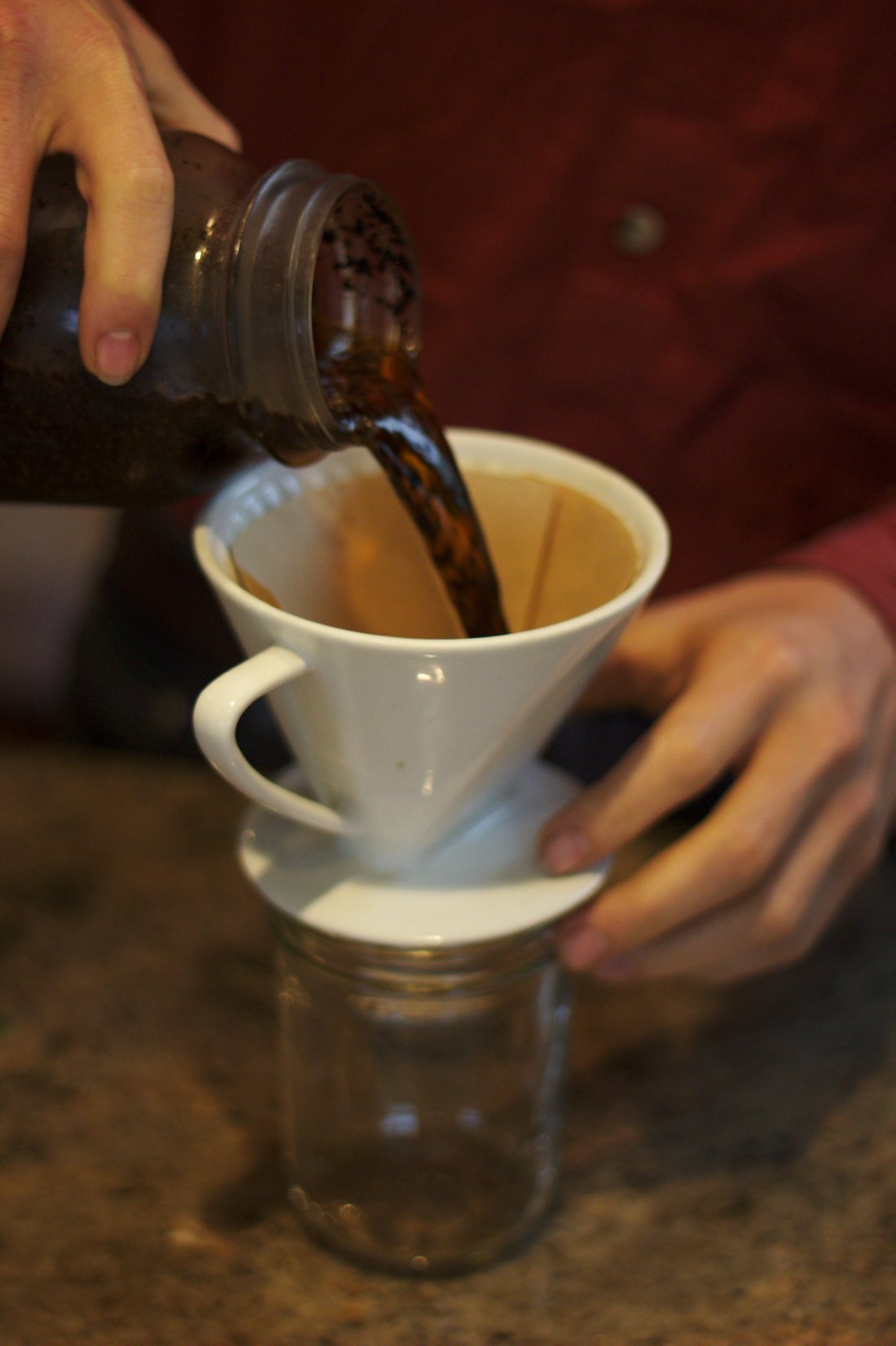 Cold brew coffee being poured from a jar through a paper filter cone into another jar