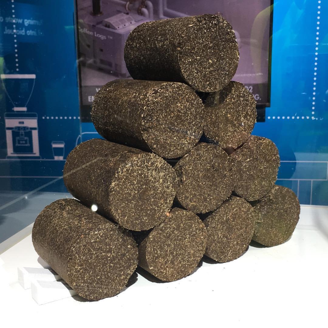A stack of short cylindrical logs pressed from dark, crumbly material, displayed under glass