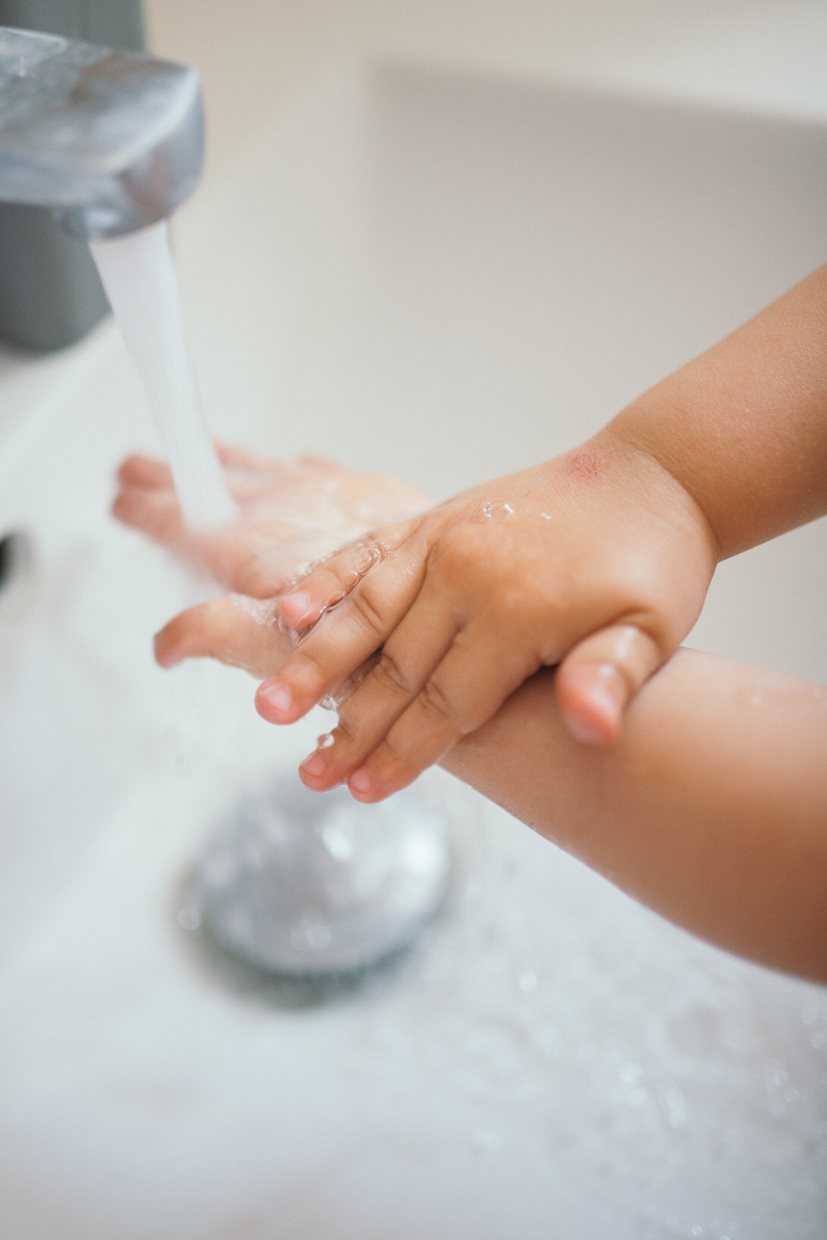 A small hand under a running tap in a white basin, water splashing