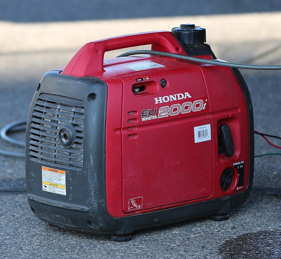 A small red portable inverter generator sitting on pavement
