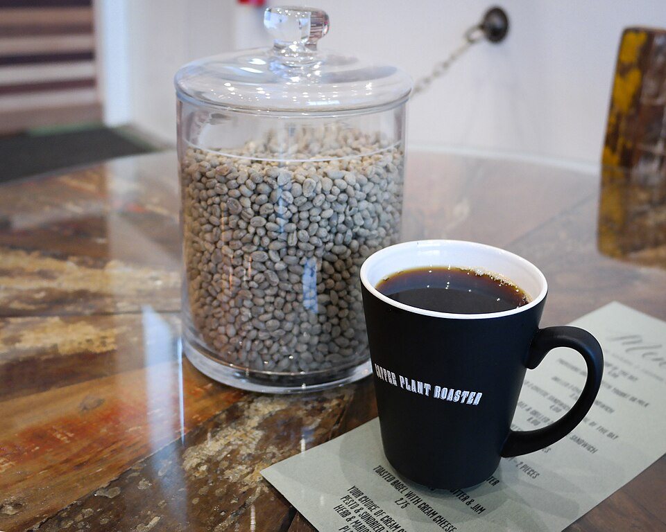 A glass jar of green coffee beans on a counter beside a black mug of brewed coffee