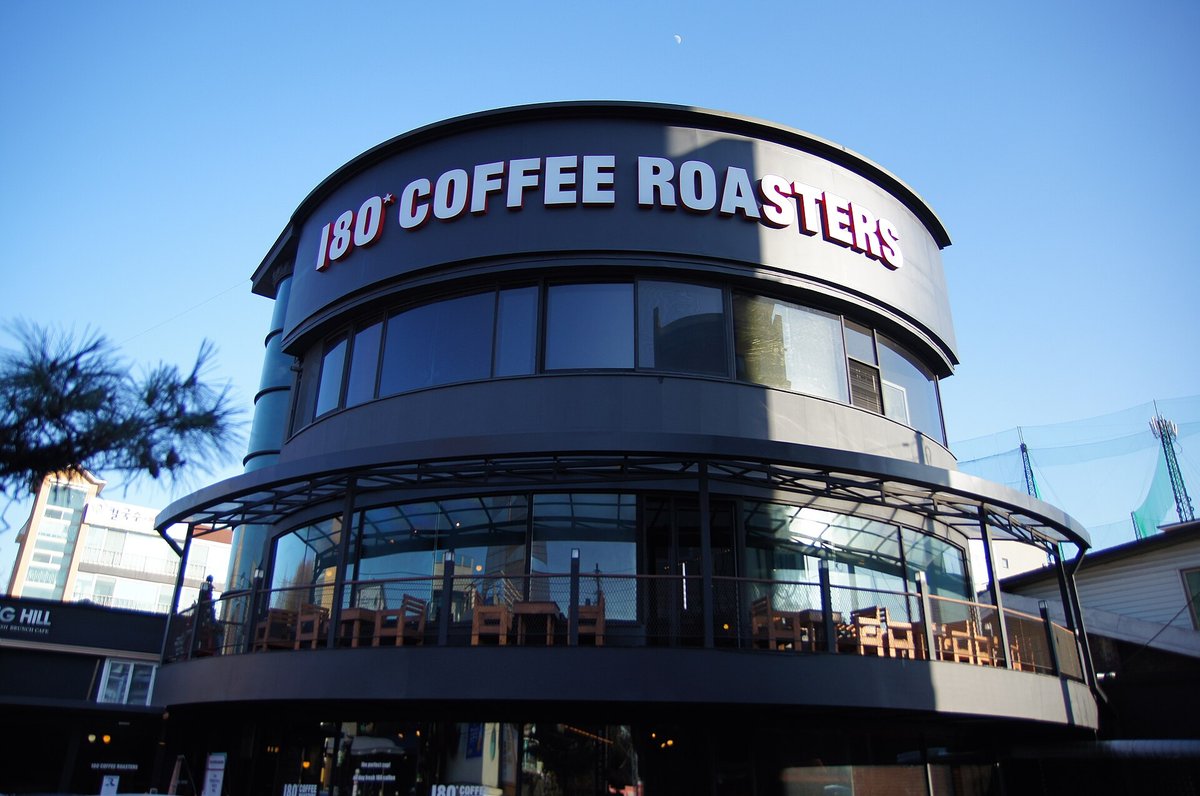 A round two-storey café building with a large sign reading 180 Coffee Roasters along its roofline, photographed against a blue evening sky