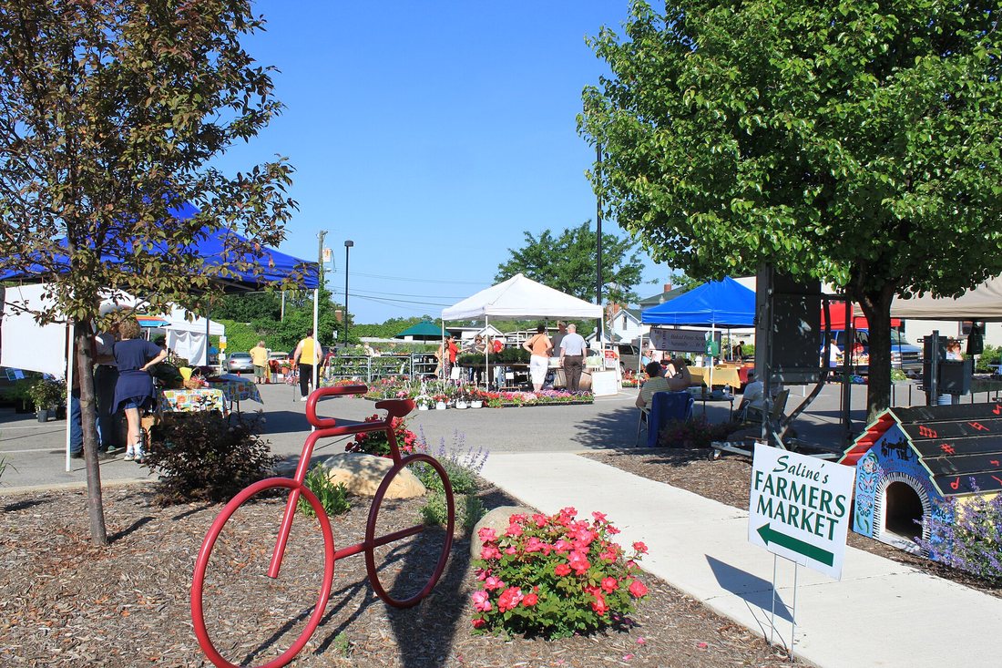The entrance to a farmers market with a painted sign, a red bicycle and canopies beyond