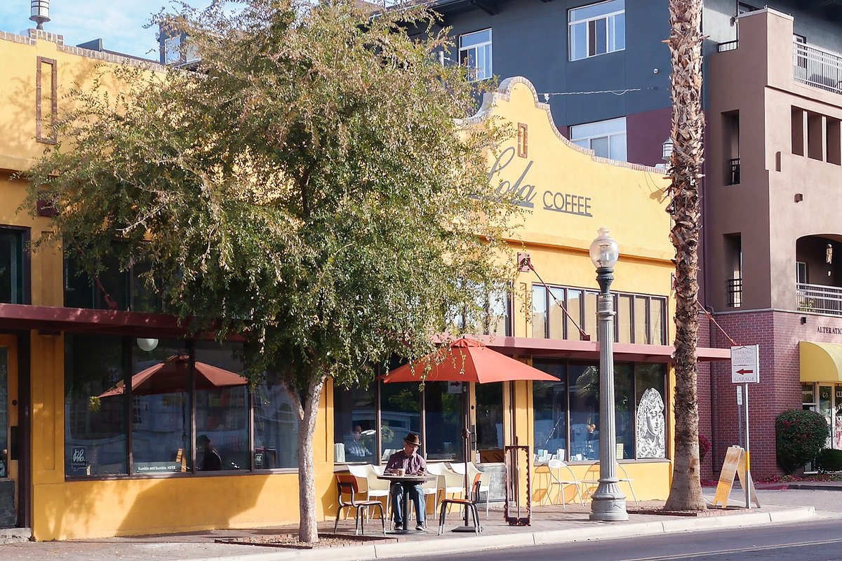 The yellow stucco front of a small café with a red umbrella over a sidewalk table and a street lamp outside