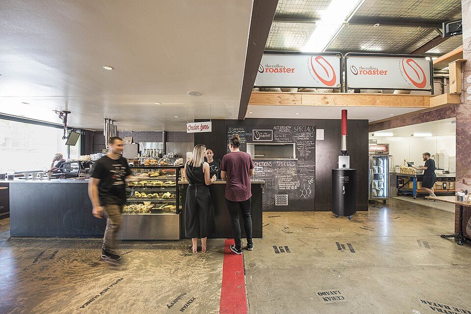The counter of a café with customers at a pastry case; signs overhead read roaster