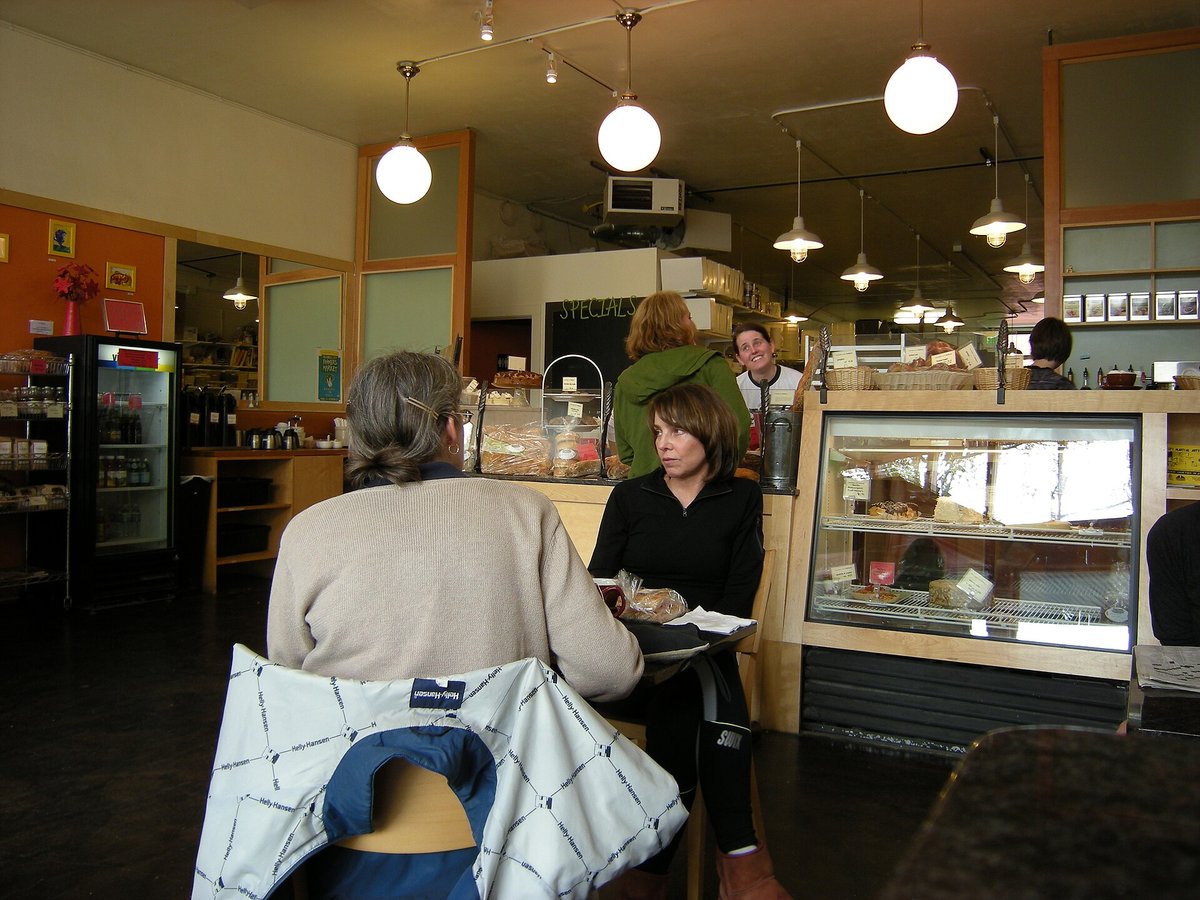 Customers at a table in a bakery café with a lit pastry case and a refrigerator of drinks behind the counter