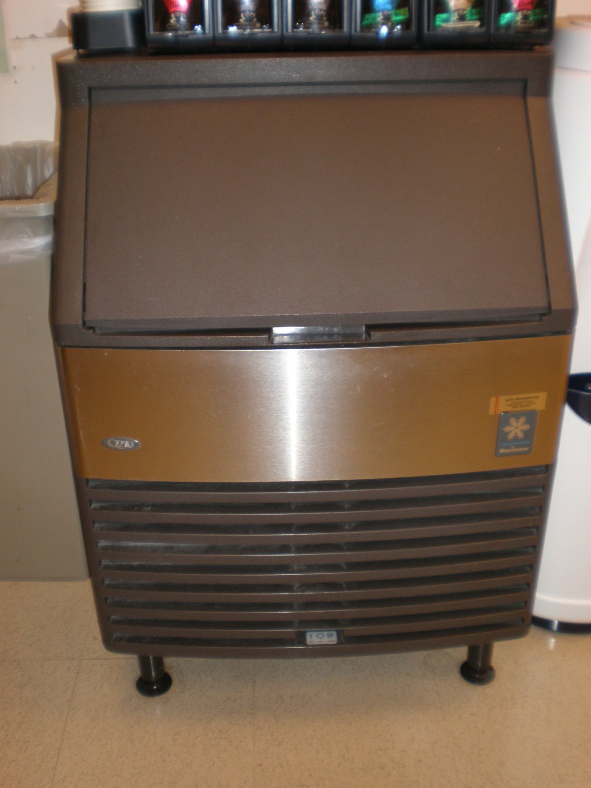 A stainless and black undercounter ice machine on a tiled floor