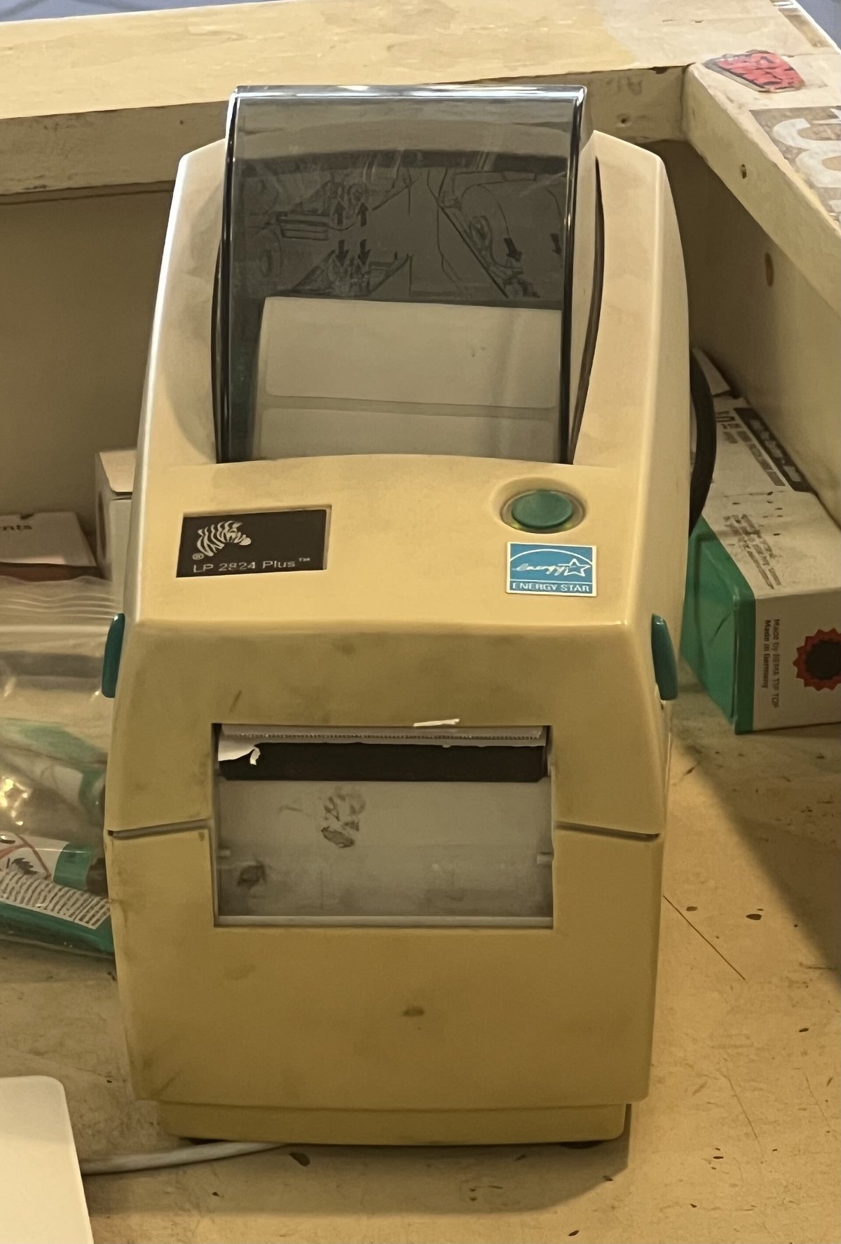 A beige thermal label printer with its lid closed, a short strip of blank label coming out of the front
