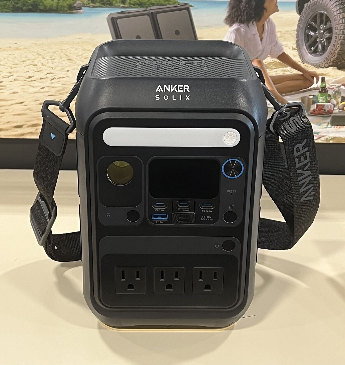 A portable power station with a carrying strap, three AC outlets on its face