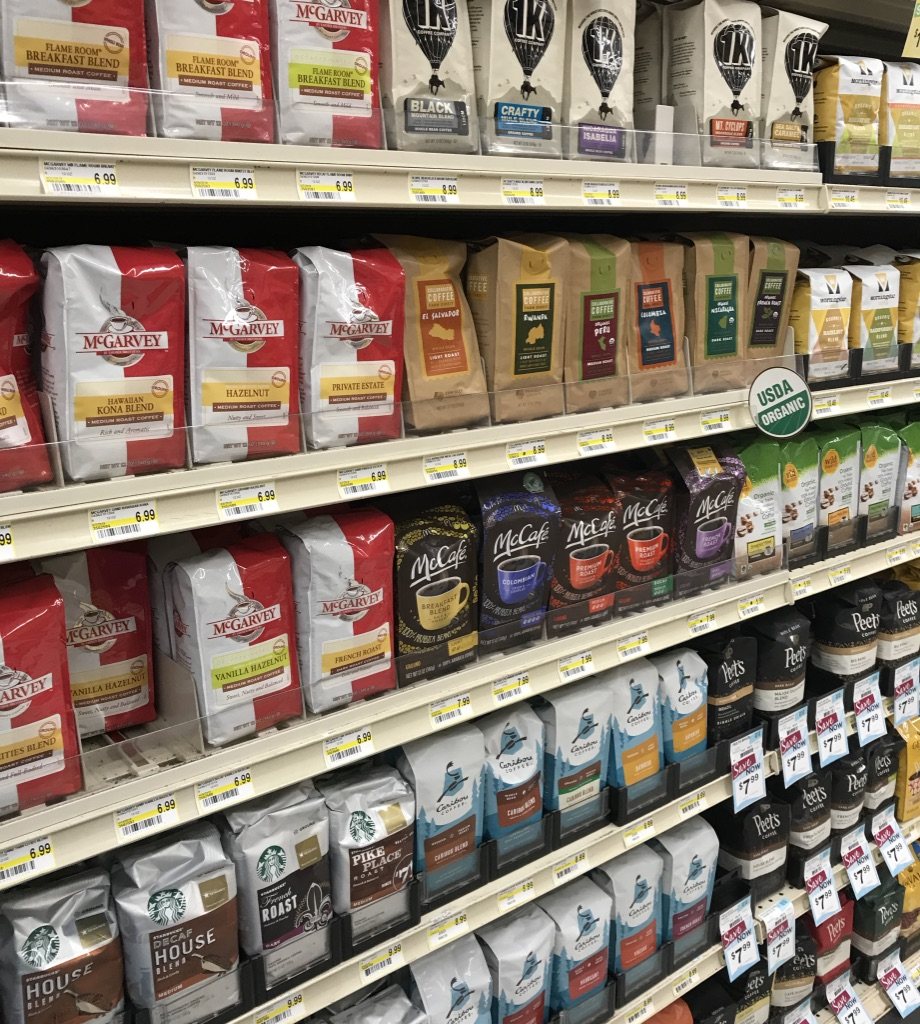 Supermarket shelves filled with bagged coffee from many brands, price tags along every shelf edge