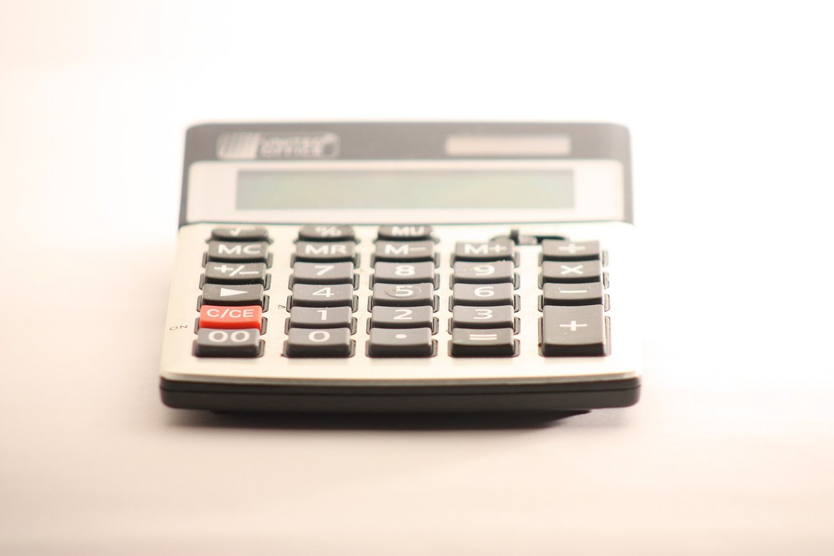 A white desktop calculator with a large grey display, lying on a white surface