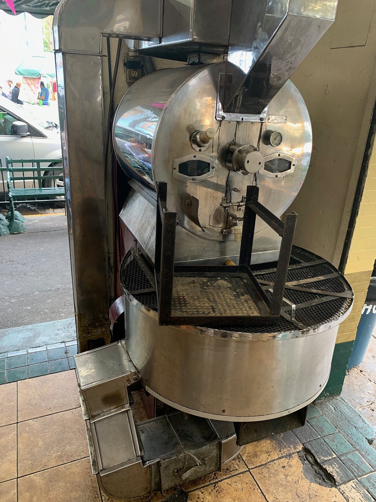 A coffee roasting drum and its exhaust pipe in a small coffee shop in Mexico City, in front of a window onto the street