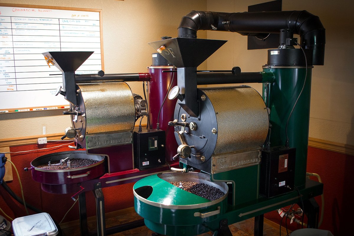 Two shop drum roasters side by side, one with a green cooling tray, in a small roastery