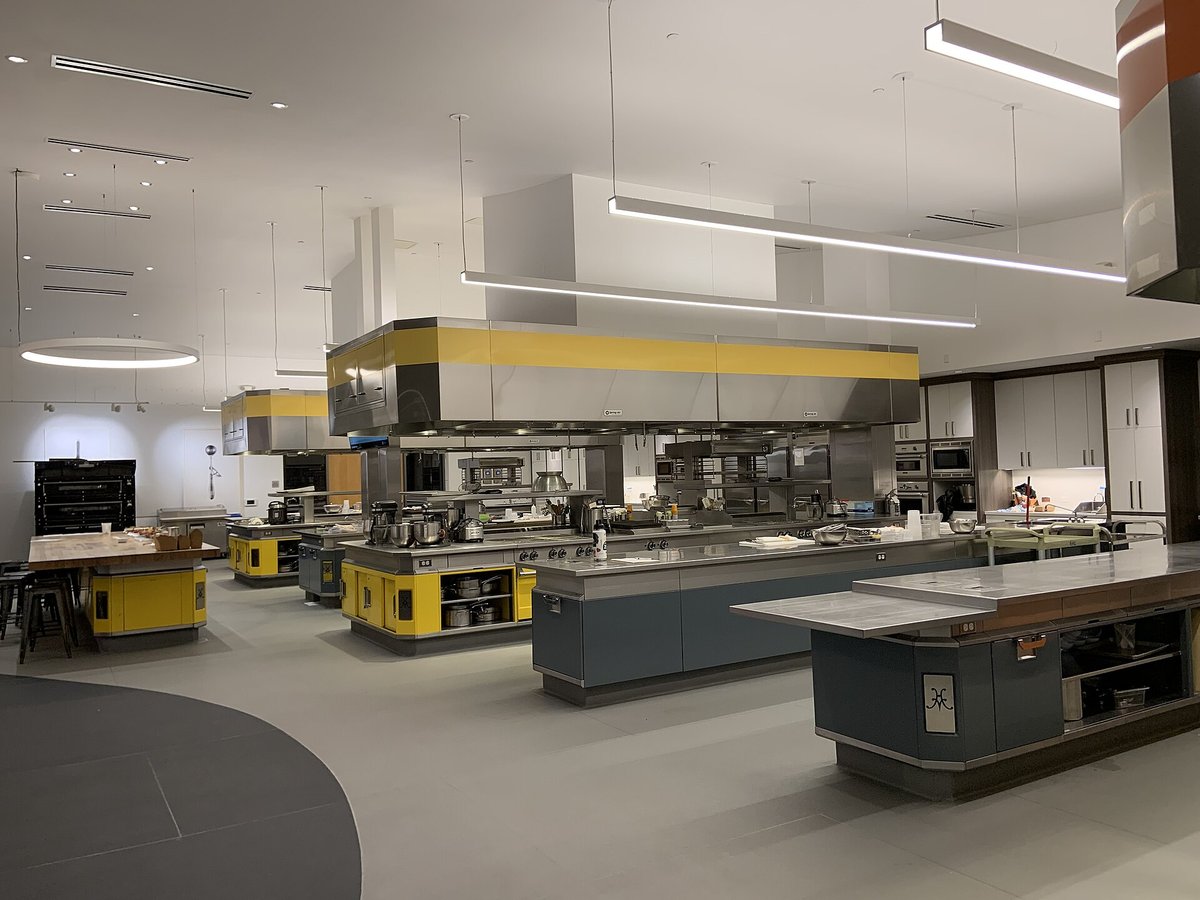 A large, bright commercial kitchen with stainless ranges, prep tables and yellow hoods