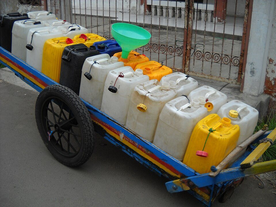 A hand cart loaded with white and yellow plastic jerrycans and a funnel