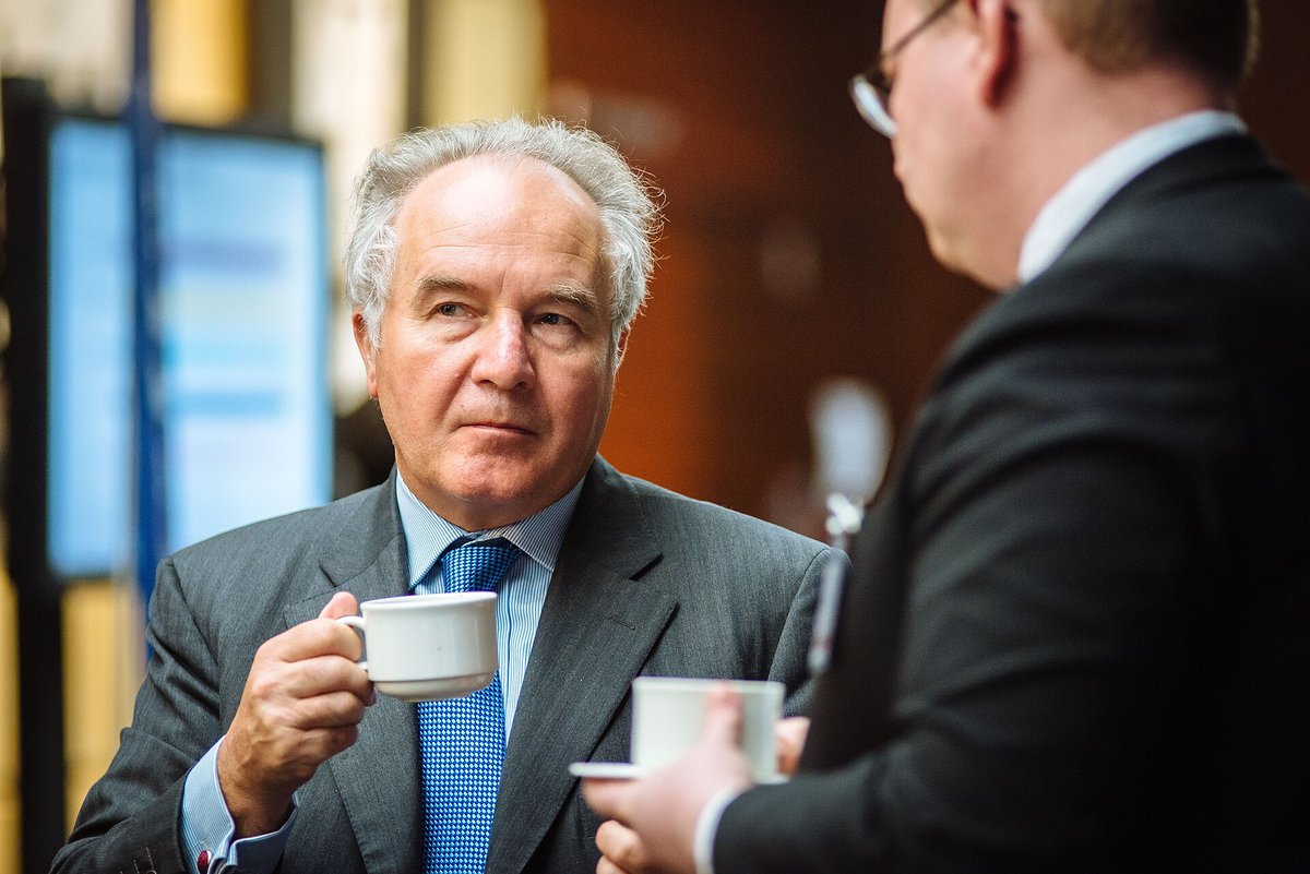 Two men in suits holding white coffee cups at a conference coffee break