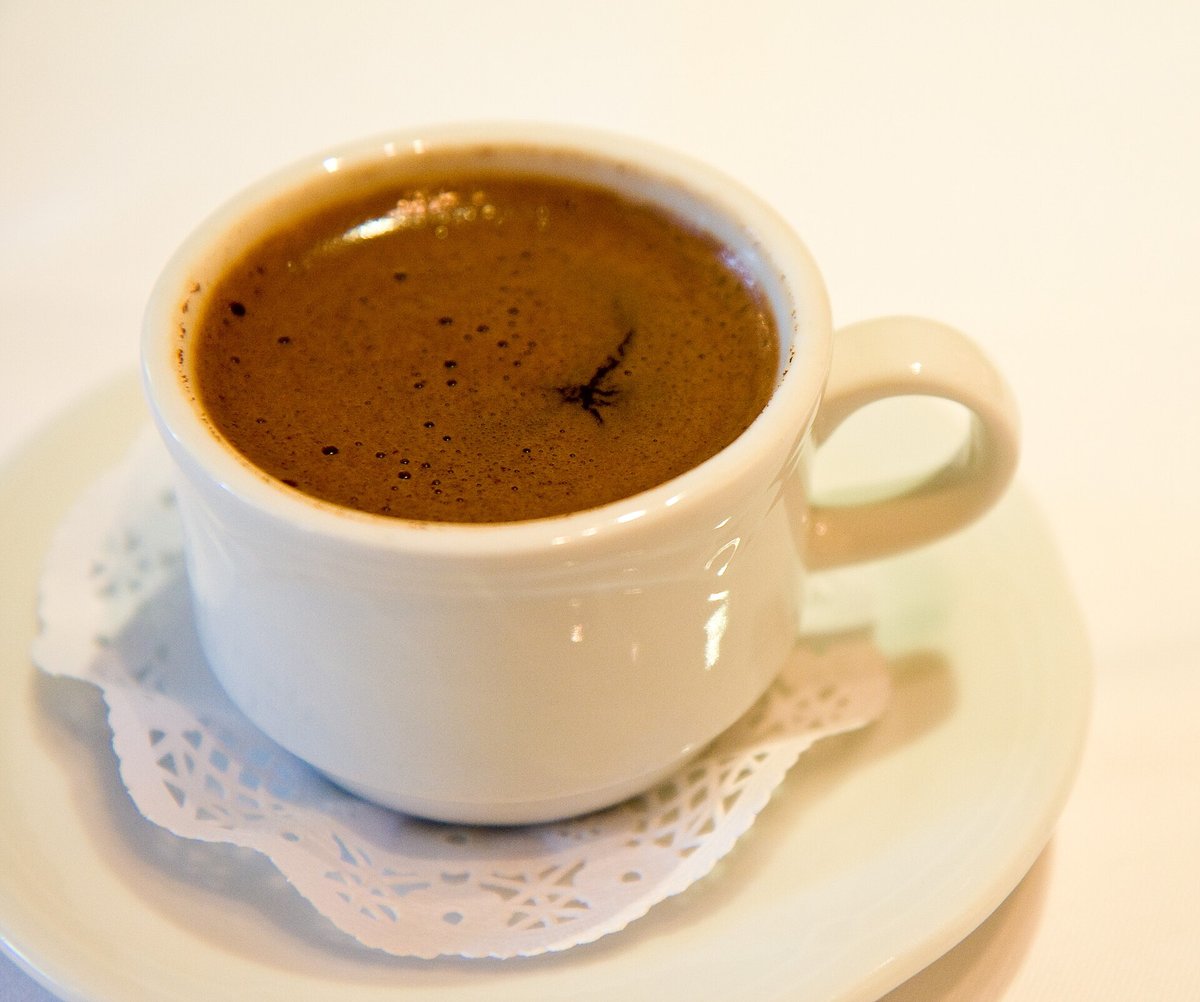 A white cup of Turkish coffee on a saucer and lace doily, its surface a fine brown foam