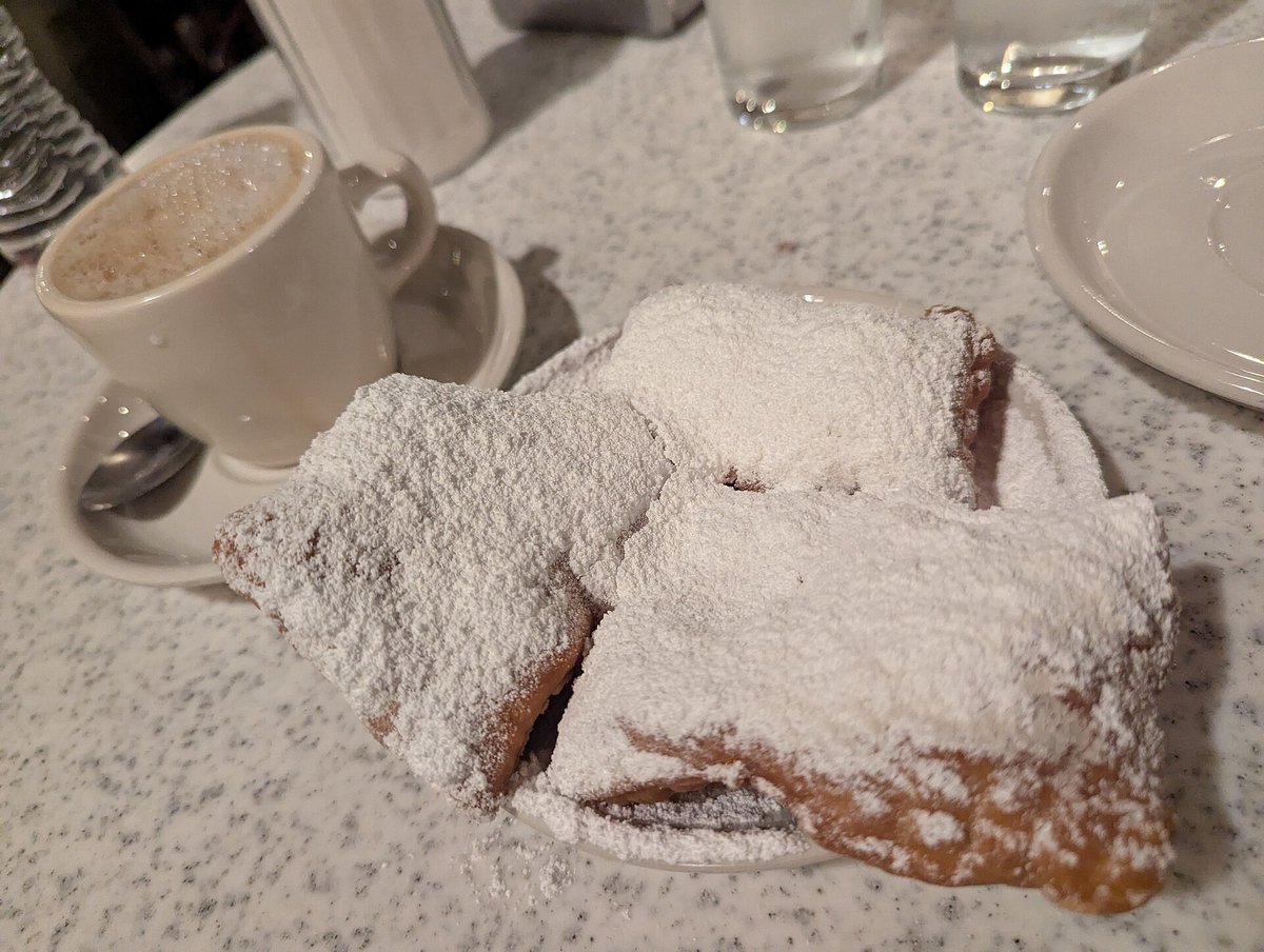 A plate of beignets heaped with powdered sugar beside a cup of café au lait on a marble table at Café du Monde in the French Market, November 2025