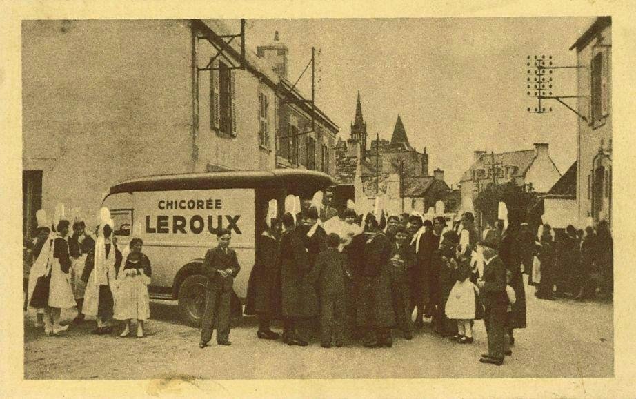 A 1910s French advertising postcard: a crowd in Breton dress around a delivery van painted "Chicorée Leroux" in the village of Penmarc'h, with the church tower behind