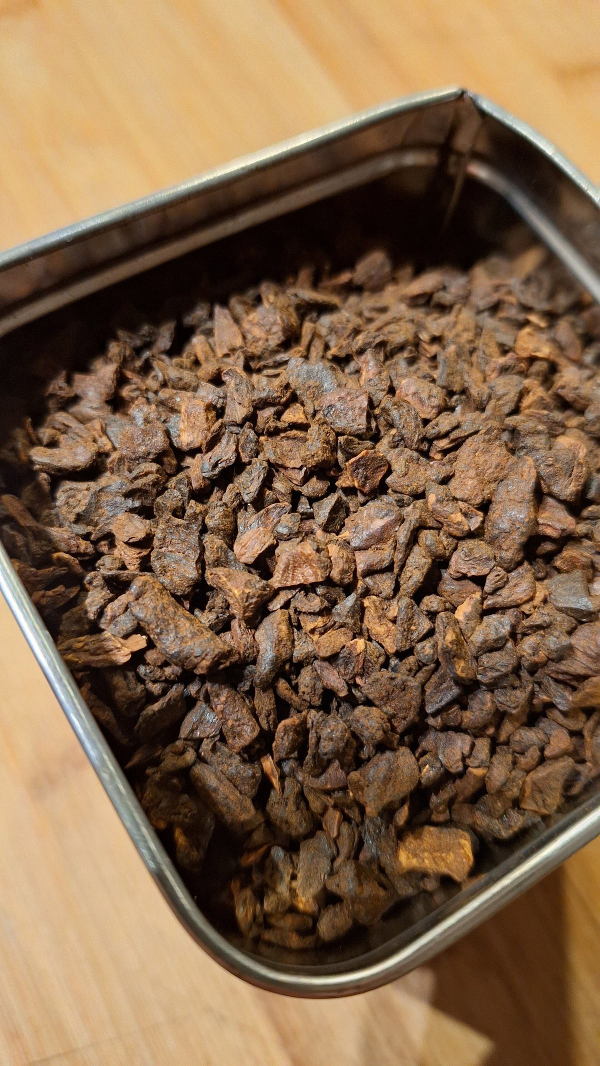 Roasted chicory granules, dark brown and glossy, in a small metal tin