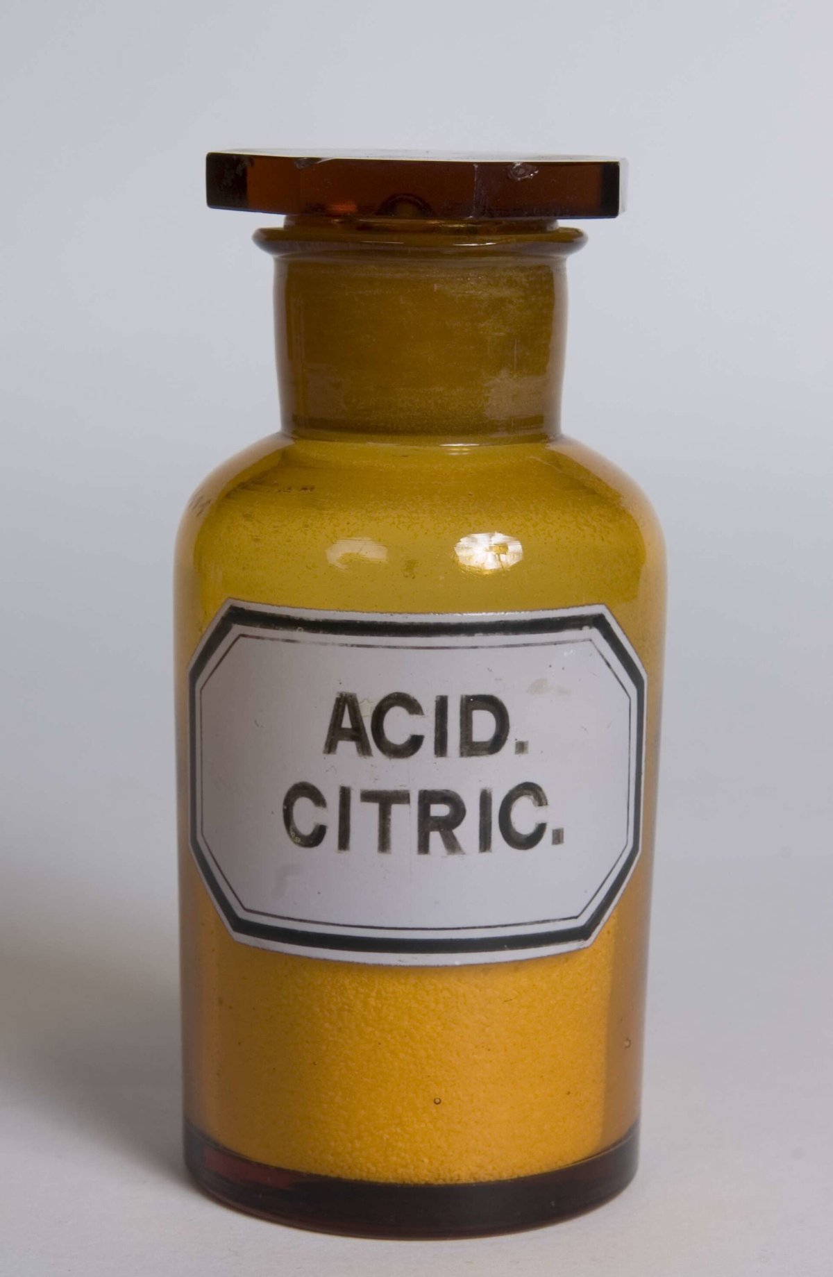 An old brown glass pharmacy jar with a label reading Acid. Citric., holding a yellowish powder