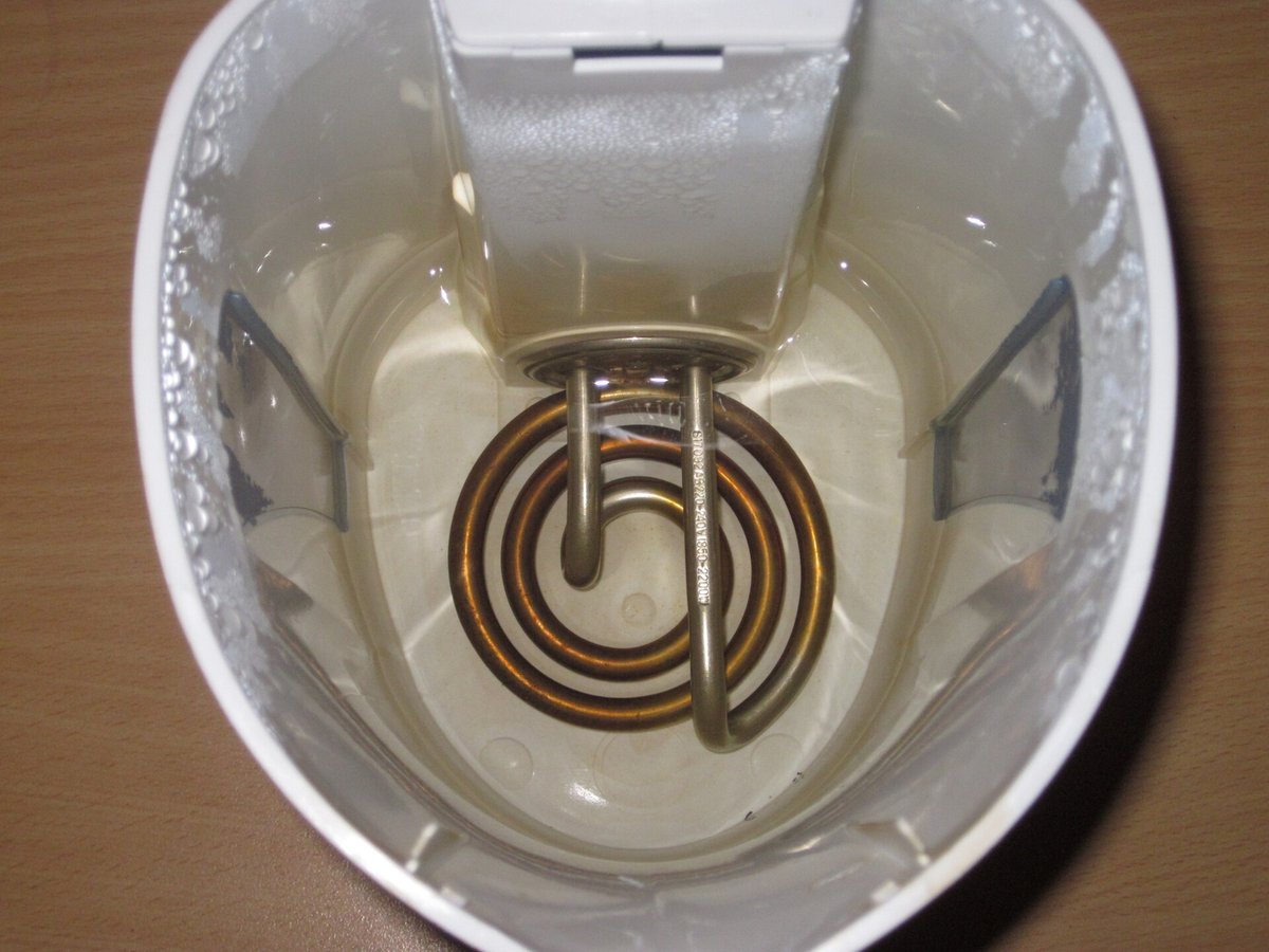 The inside of a white electric kettle looking down at its coiled heating element, the element and water discoloured