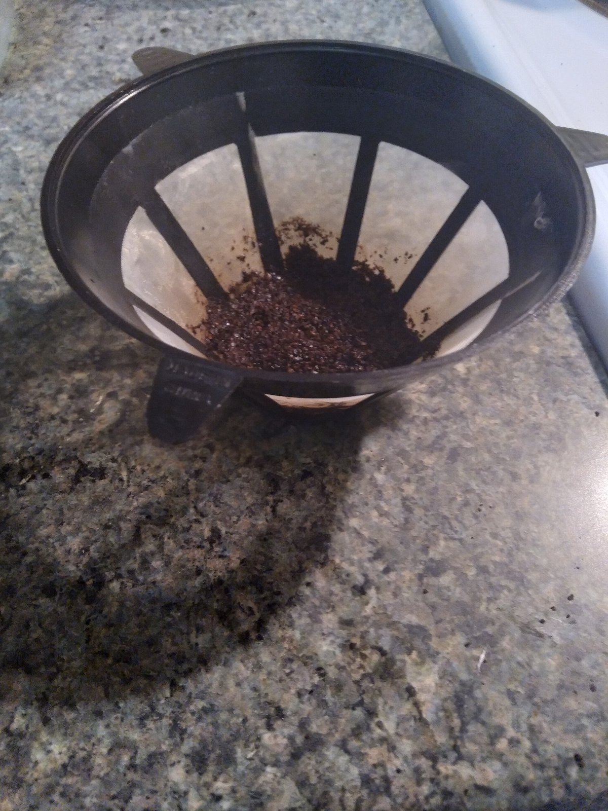 A gold-coloured mesh coffee filter basket on a granite counter, with used grounds still inside