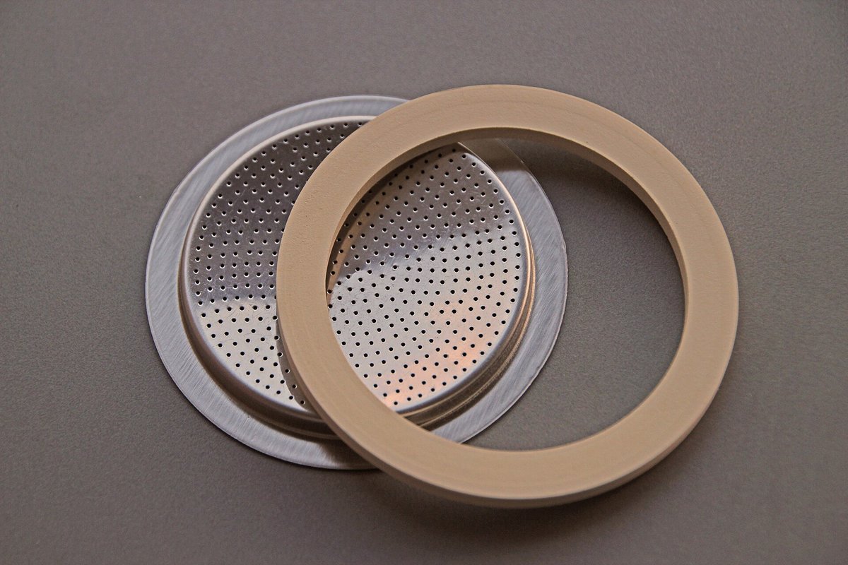 A Bialetti spare-parts set: a pale rubber gasket ring lying on a perforated metal filter plate