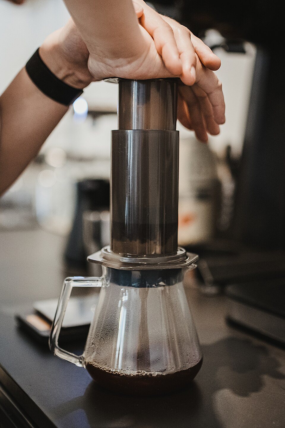 Hands pressing down the plunger of an AeroPress standing on a glass server