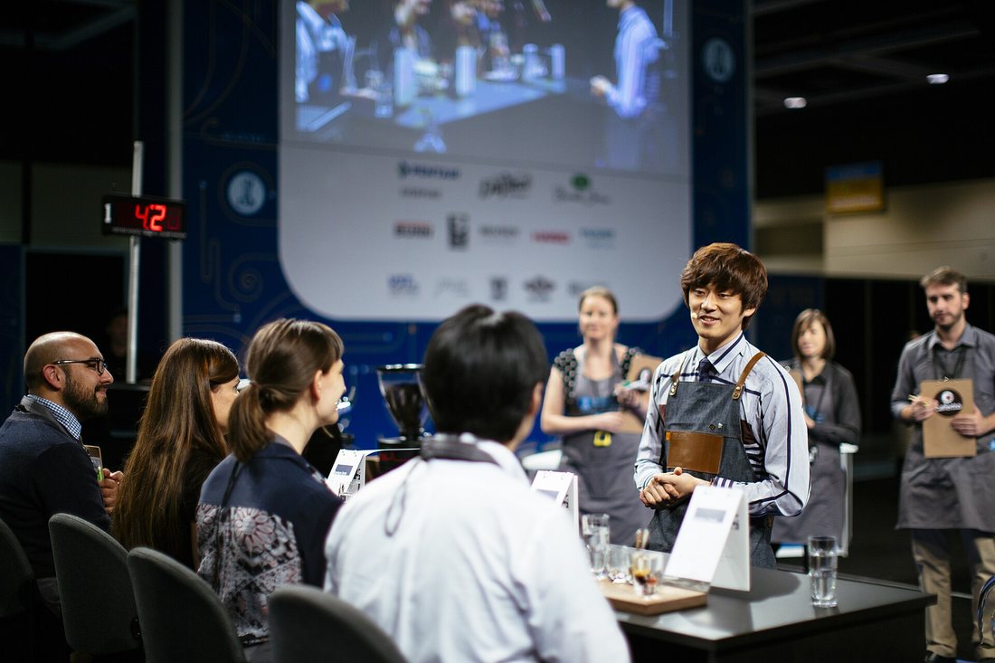 A competitor stands talking to four seated judges on a competition stage