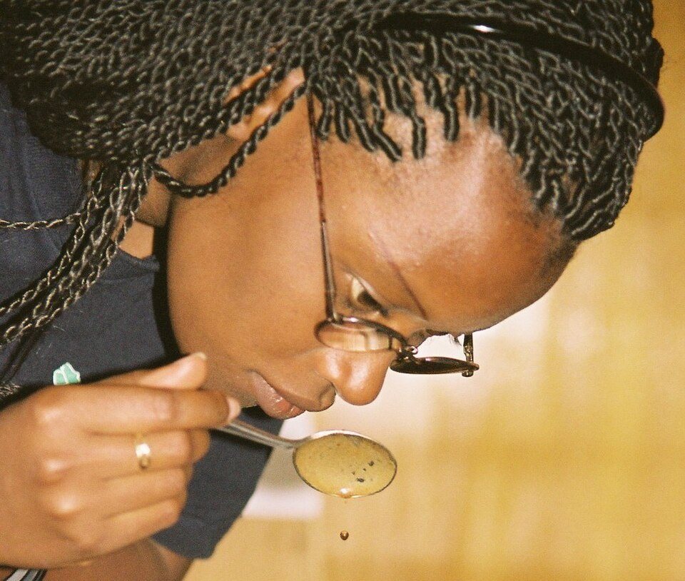 Close view of a woman in glasses drawing coffee from a round spoon held at her lips, drops falling from the spoon