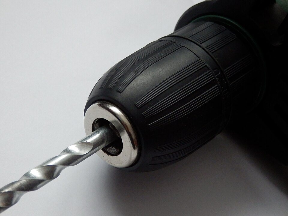 The black ribbed sleeve of a keyless drill chuck, its three steel jaws closed on a twist bit