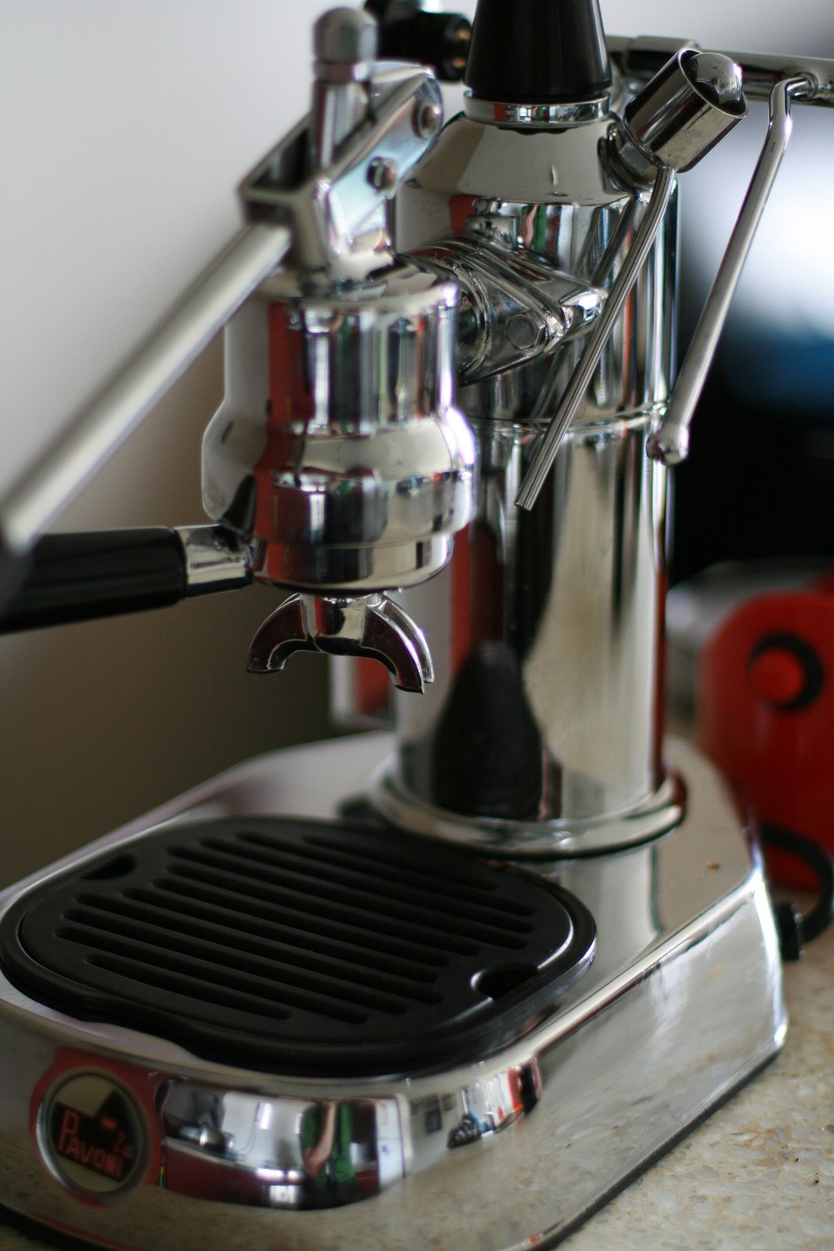 A chrome La Pavoni Europiccola lever machine with its tall lever raised and a black drip tray, photographed from the side