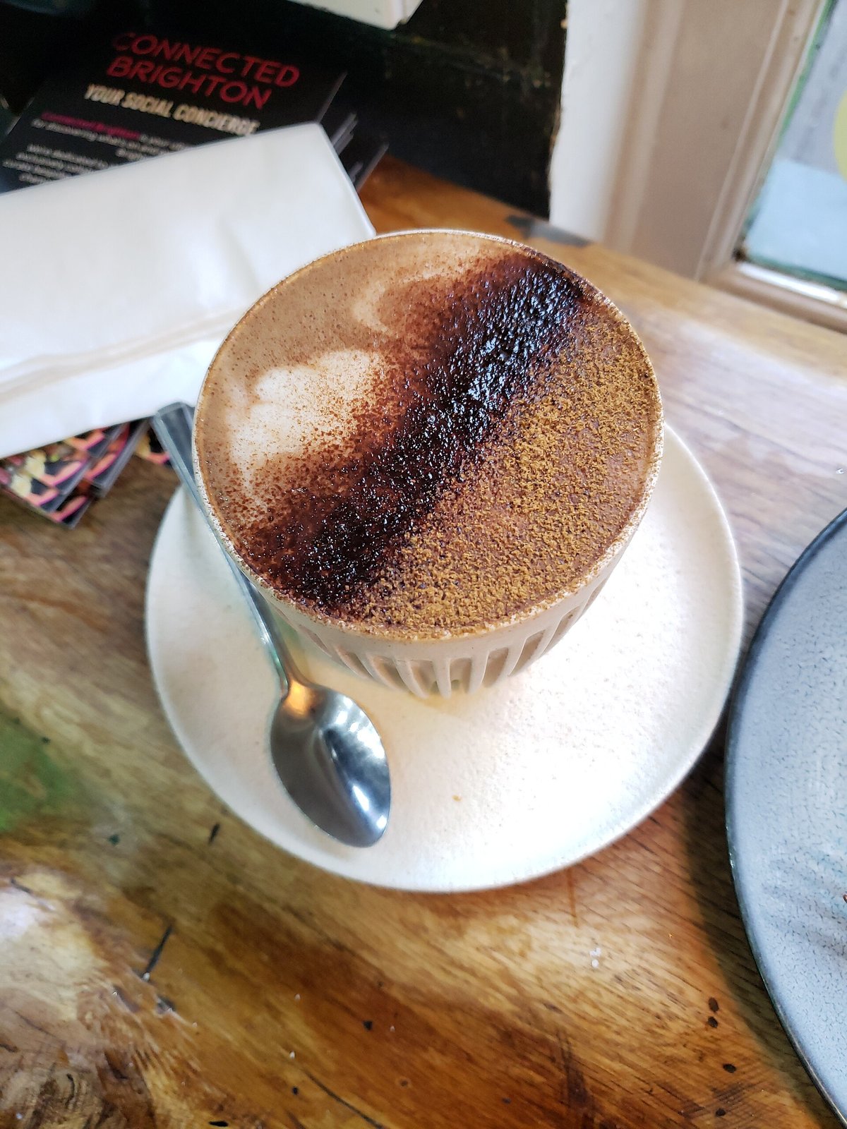A cup of gingerbread mocha with a brown, dusted foam top, on a saucer on a wooden table