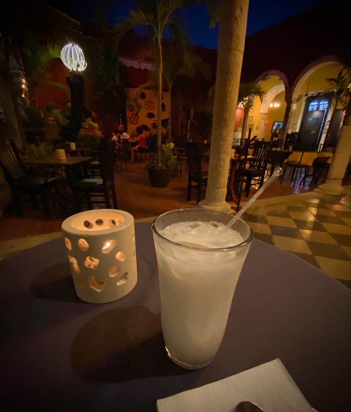 A tall glass of milky white horchata on a café table at night, beside a candle holder