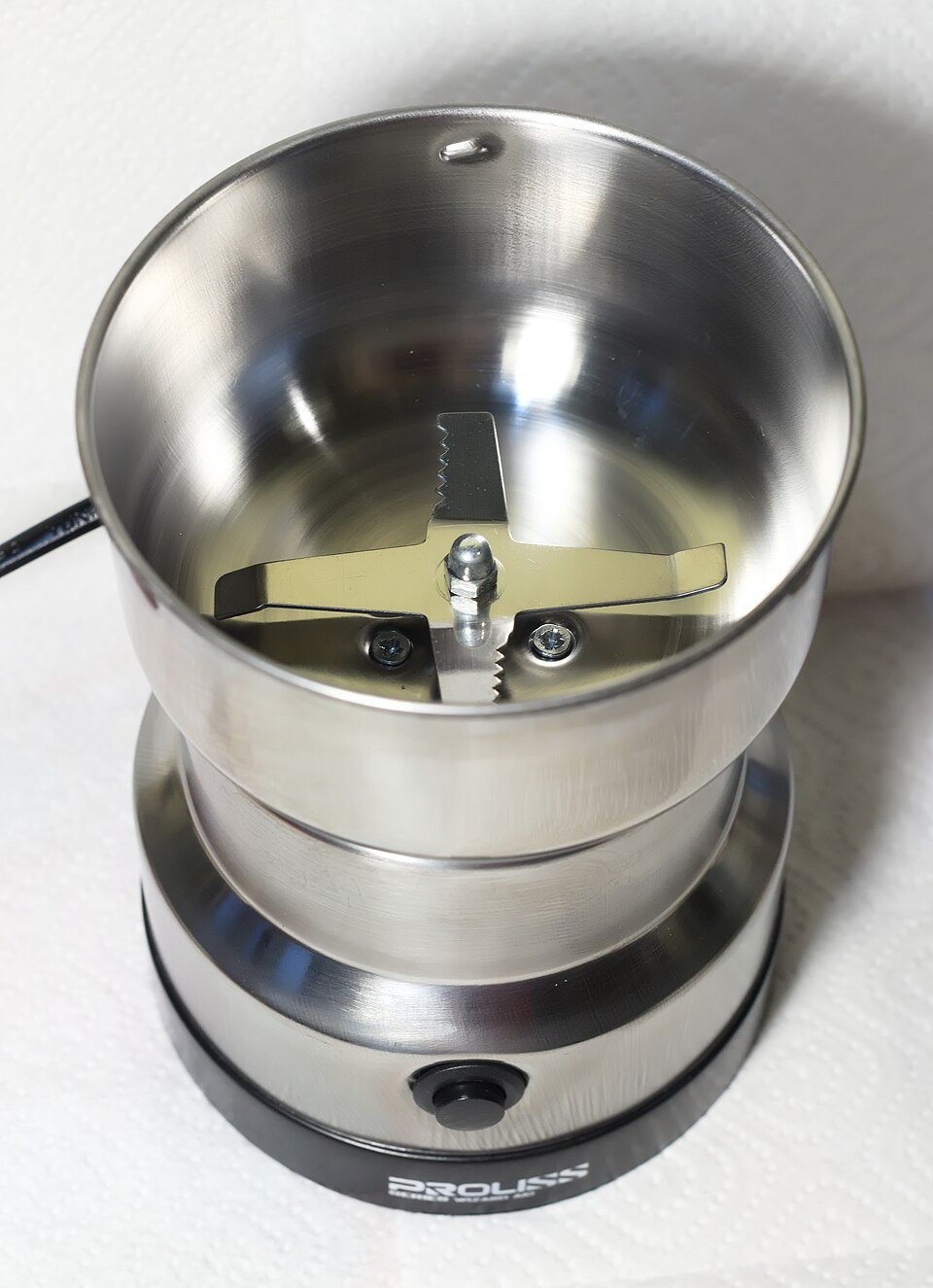 Looking down into a small electric blade grinder: a steel cup with a two-armed blade at the bottom