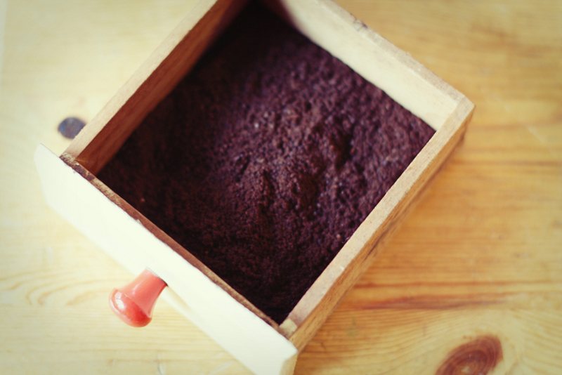 A wooden drawer pulled from a hand mill, full of freshly ground coffee