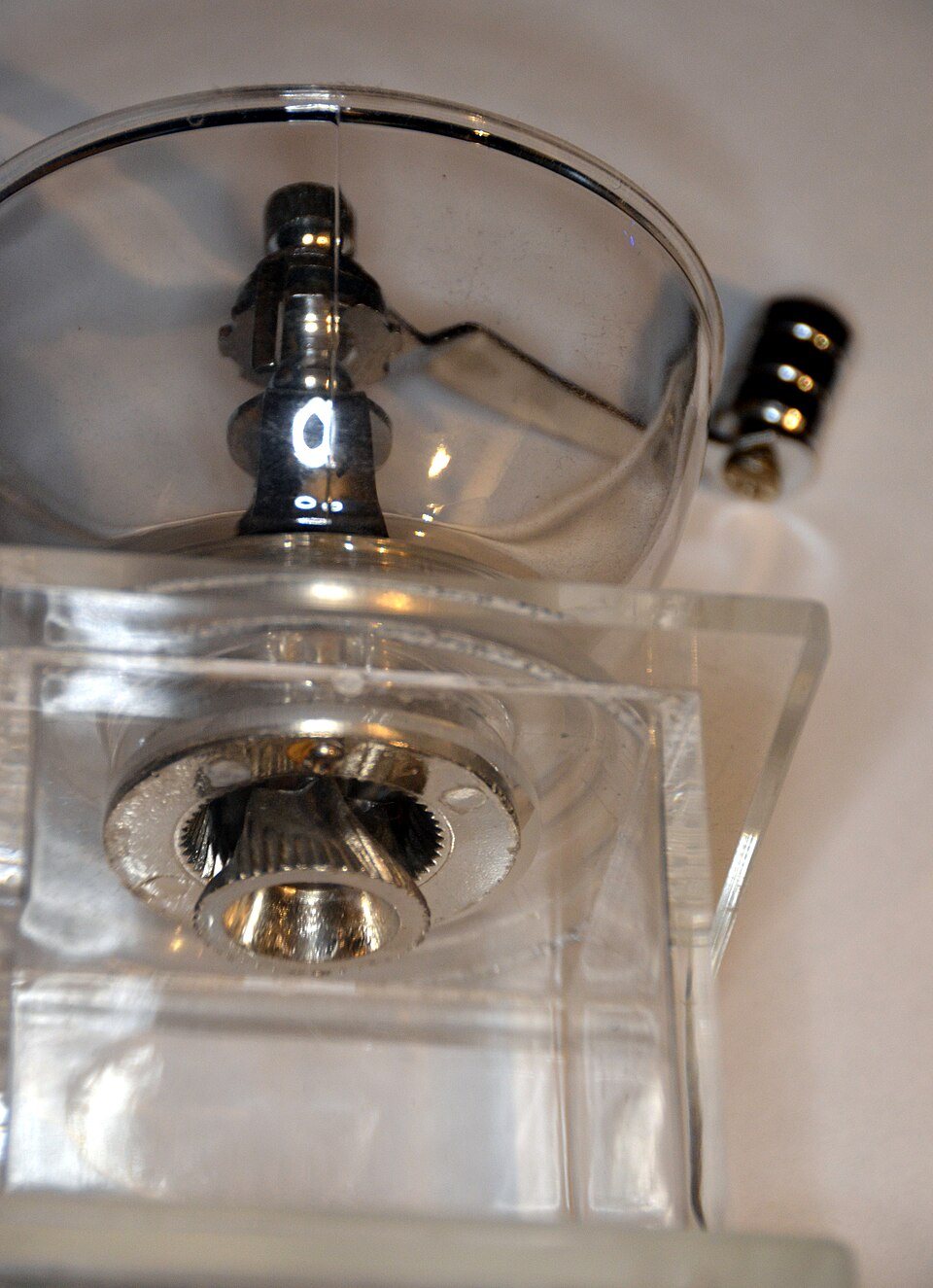 The burr of a hand grinder seen through its clear body: a small steel cone with spiral teeth sitting inside a toothed ring