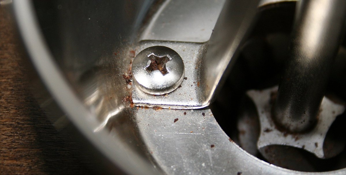 Looking down into a hand grinder with the hopper open: the cone-shaped inner burr inside the outer burr, with a few grounds clinging to them