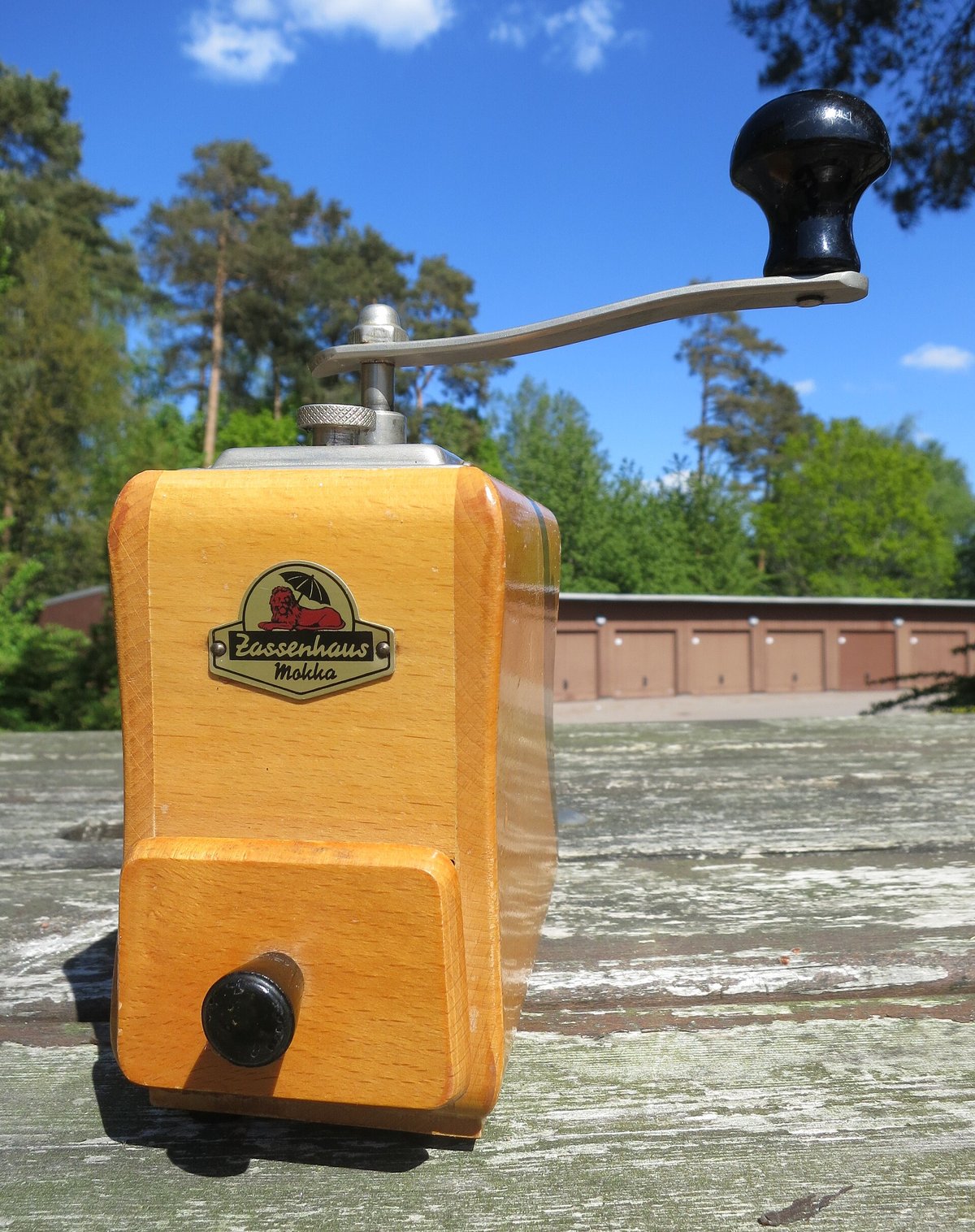 An old wooden box grinder with a brass crank, standing on a rock in the sun
