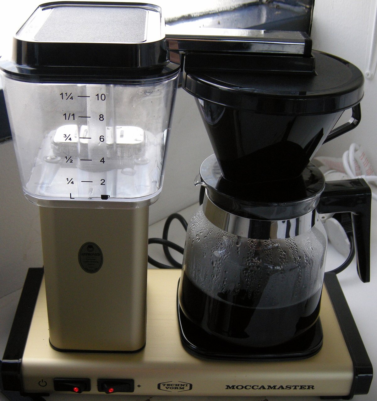 A Moccamaster drip coffee maker with its water tank and a glass carafe on the hot plate